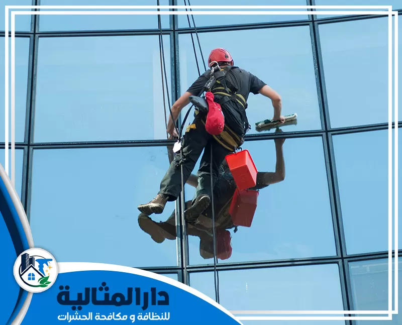 تنظيف الواجهات الزجاجية بالبخار بالبخار بالقطيف | 0598198483 | دار المثالية رجل ينظف النوافذ معلقاً بحبل، يعرض خدمات تنظيف النوافذ الاحترافية في القطيف.